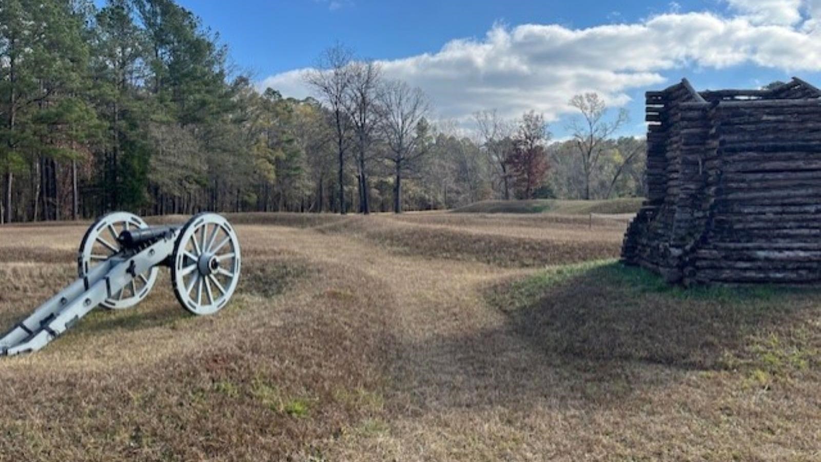 A wooden tower stands in a field next to a cannon.