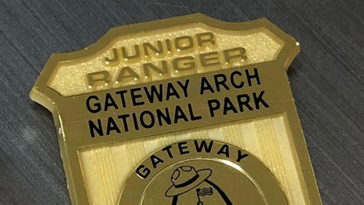 a shiny golden badge that says Gateway Arch National Park Junior Ranger