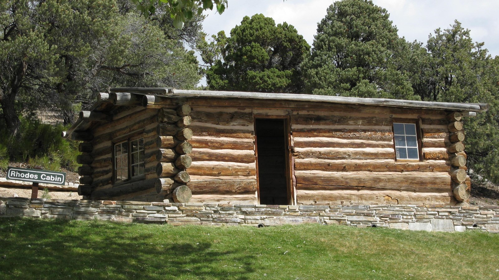 A brown log cabin with an open door leaving a dark hole in the side near a pane glass window.