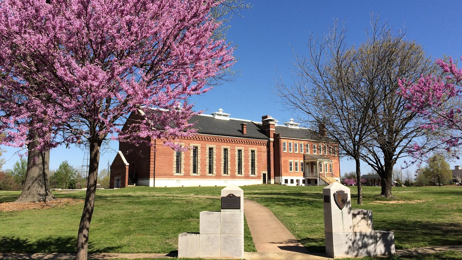 Red brick visitor center in morning sun light. Trees with pink blooms in the foreground.