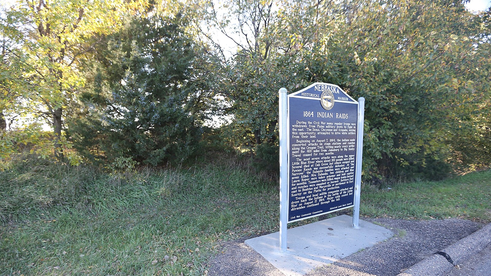 A upright sign sits in front of a wooded area.