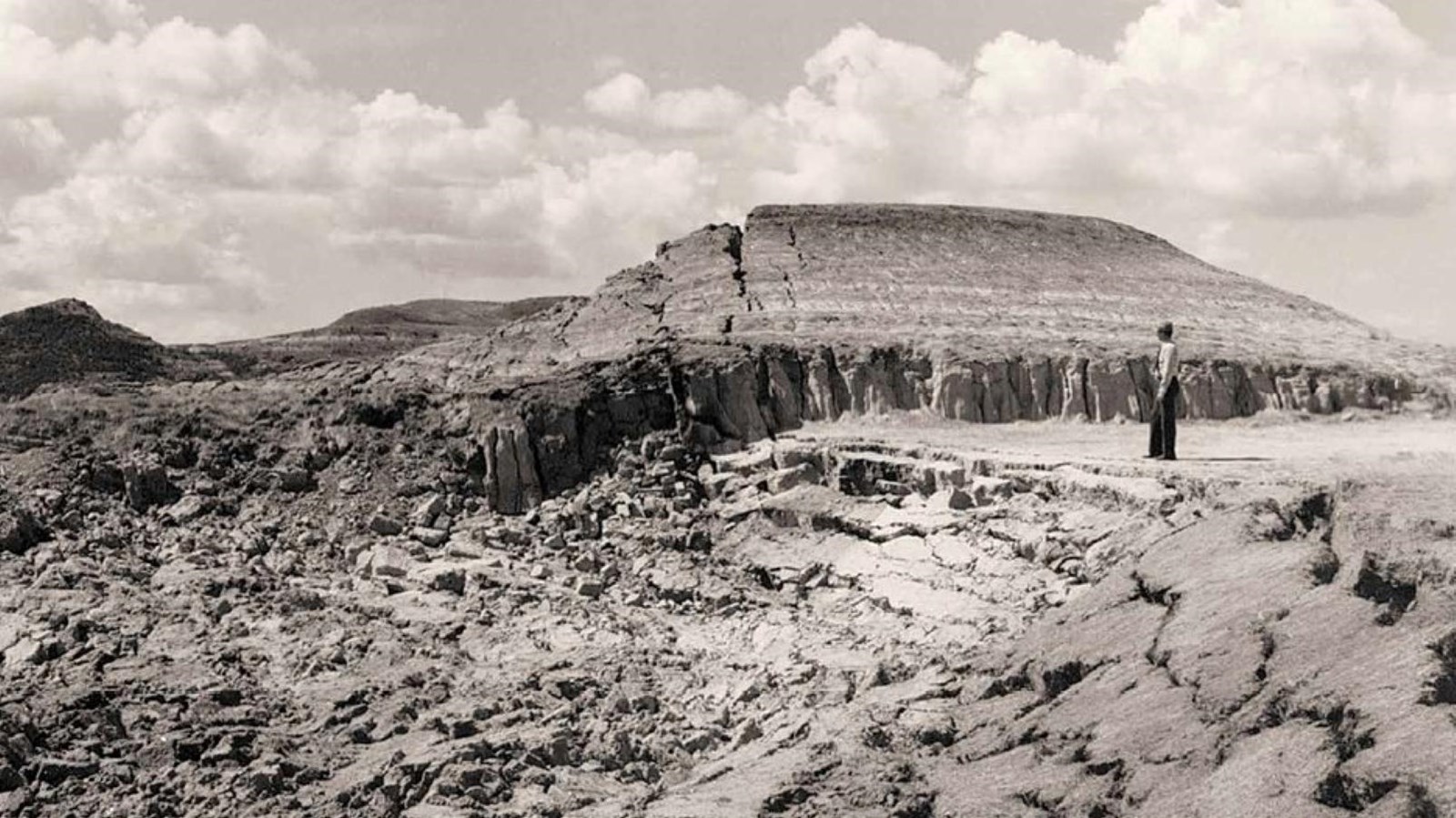 A black and white photo of a person standing at the edge of a collapse caused by a burning coal seam