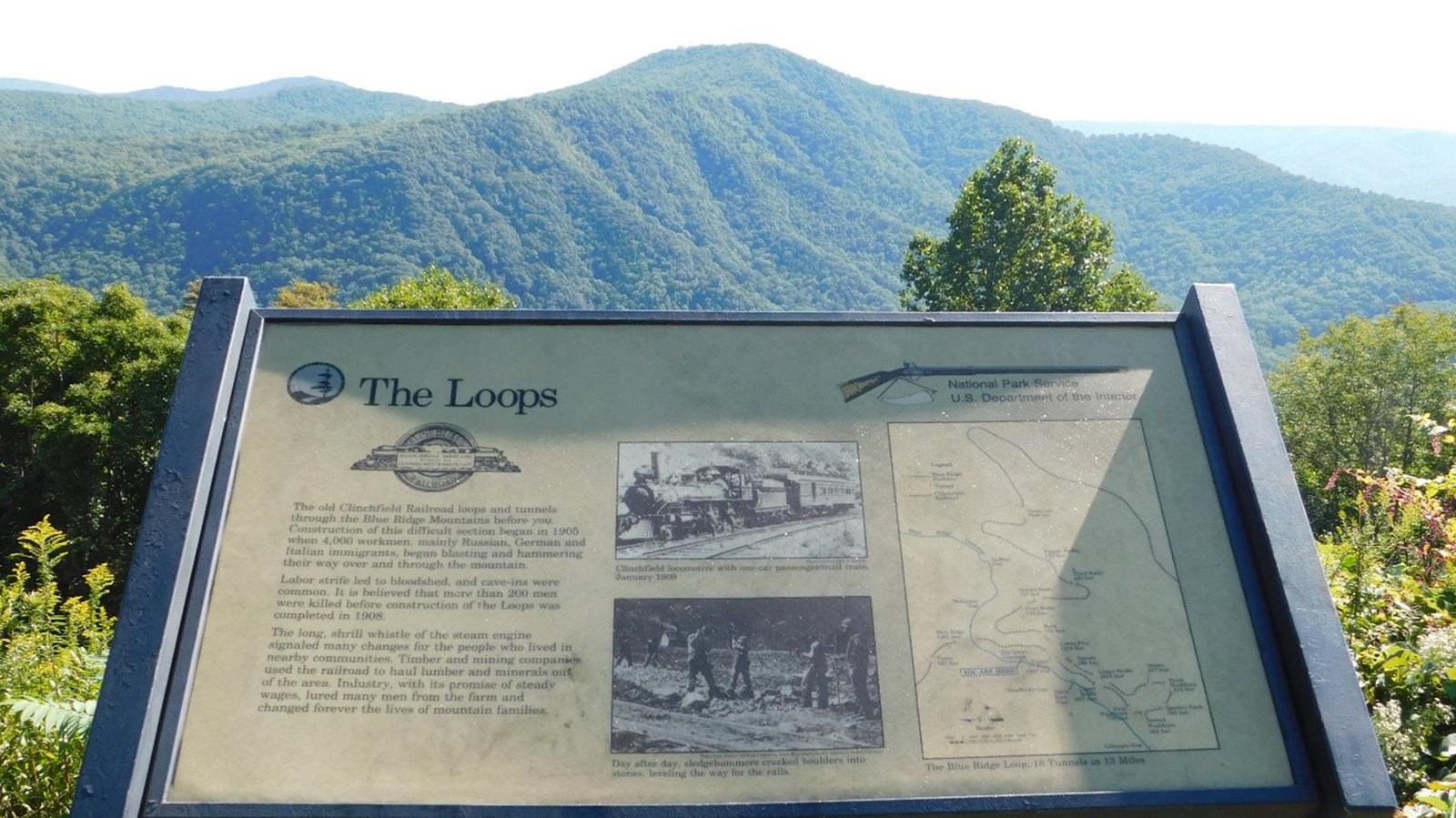 An exhibit panel sits in a grassy area with mountains in the background