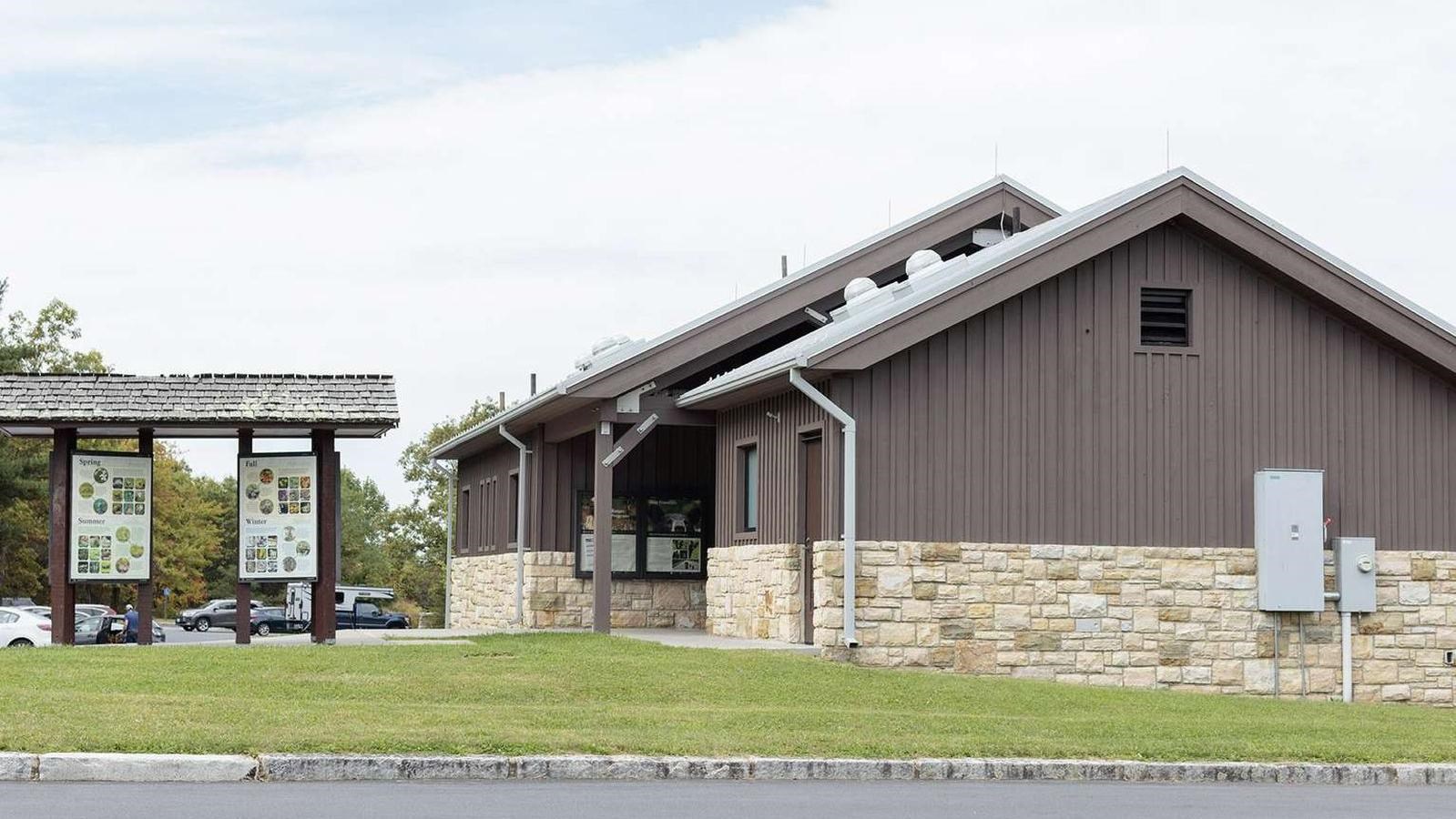 A building with interpretive panels outside surrounded by a parking area.