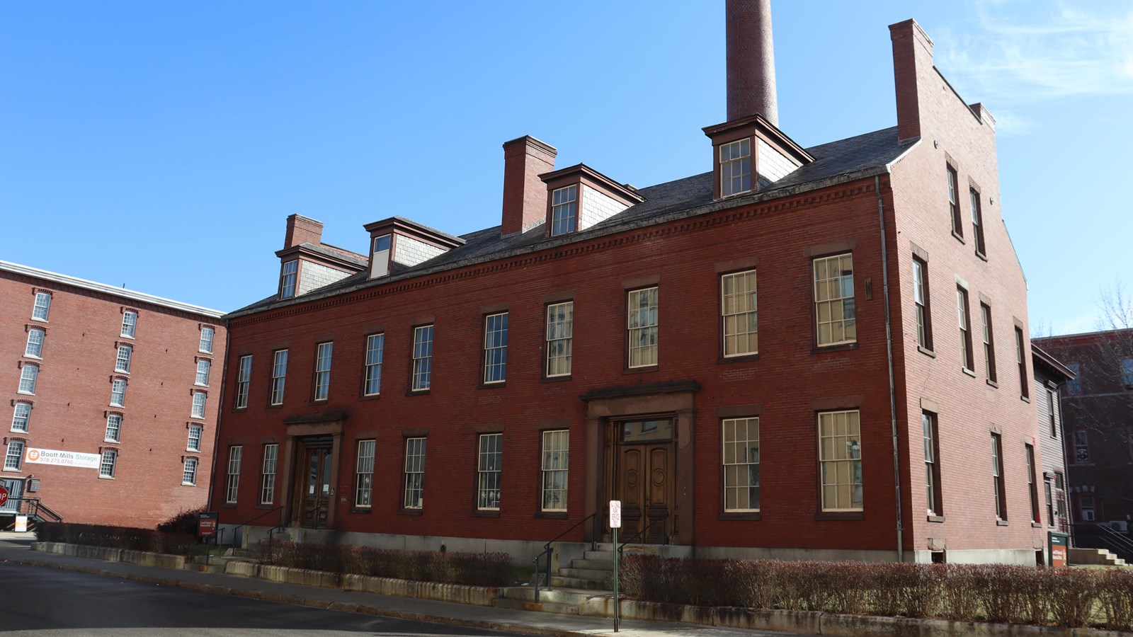 A brick building with two floors of windows, there are two main doors framed with a tan stone.