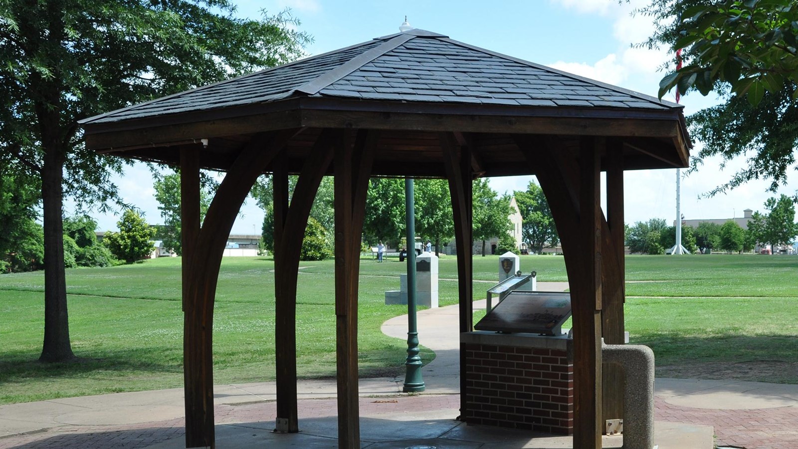 Wooden gazebo with wayside and water fountain. Green grass of the parade ground in back ground.
