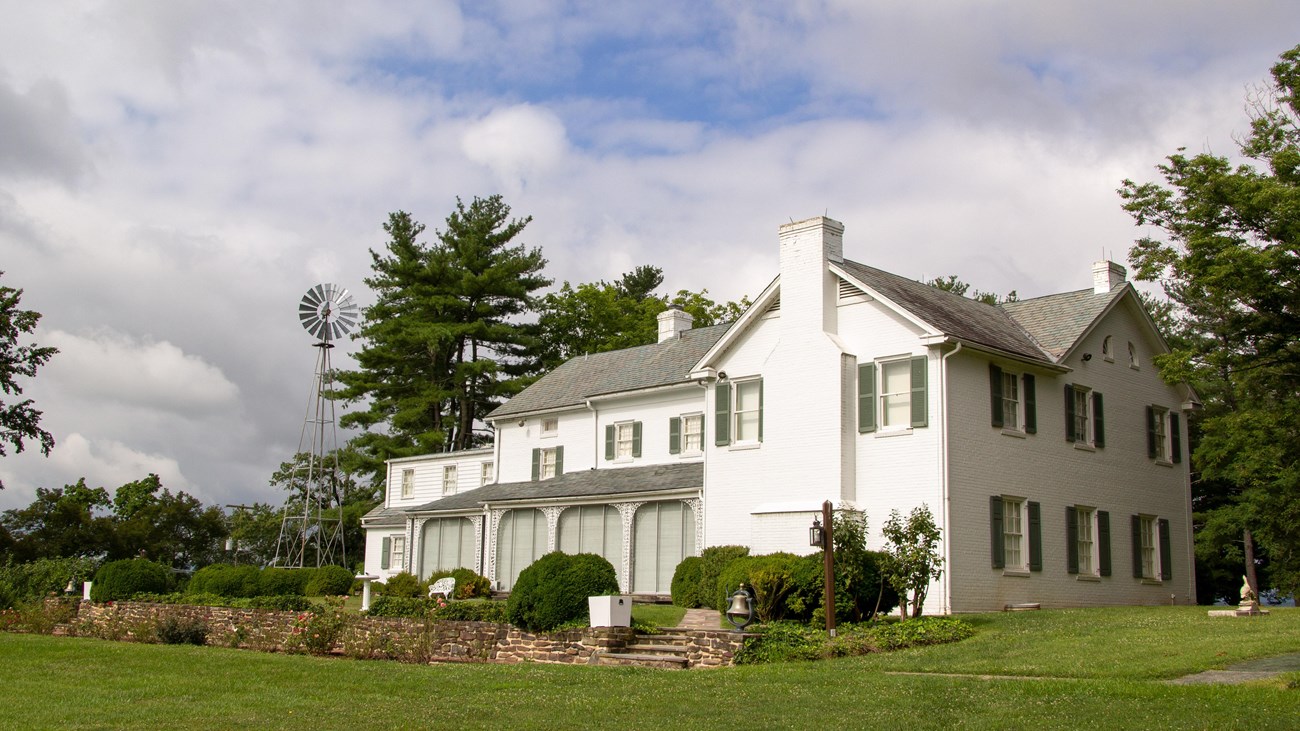 A white brick home sits underneath a blue sky with green grass and plants in the foreground