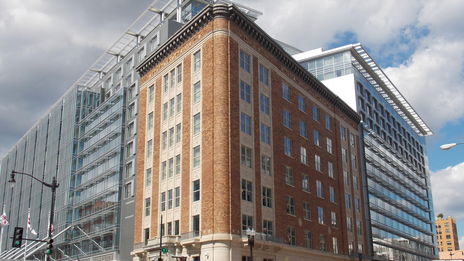 A seven story brick building forms the corner of a city block and is connected to a glass building.