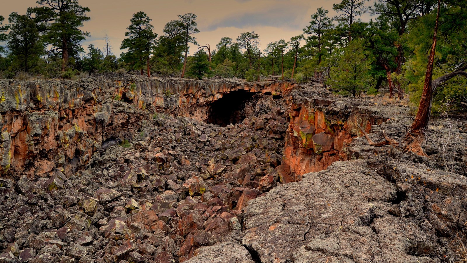 A deep trench of rubbly lava rock leads to a lava tube cave.