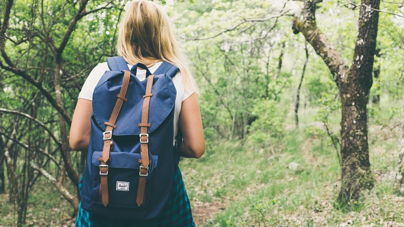 a woman with blonde hair and blue backpack walking away on a trail in the woods