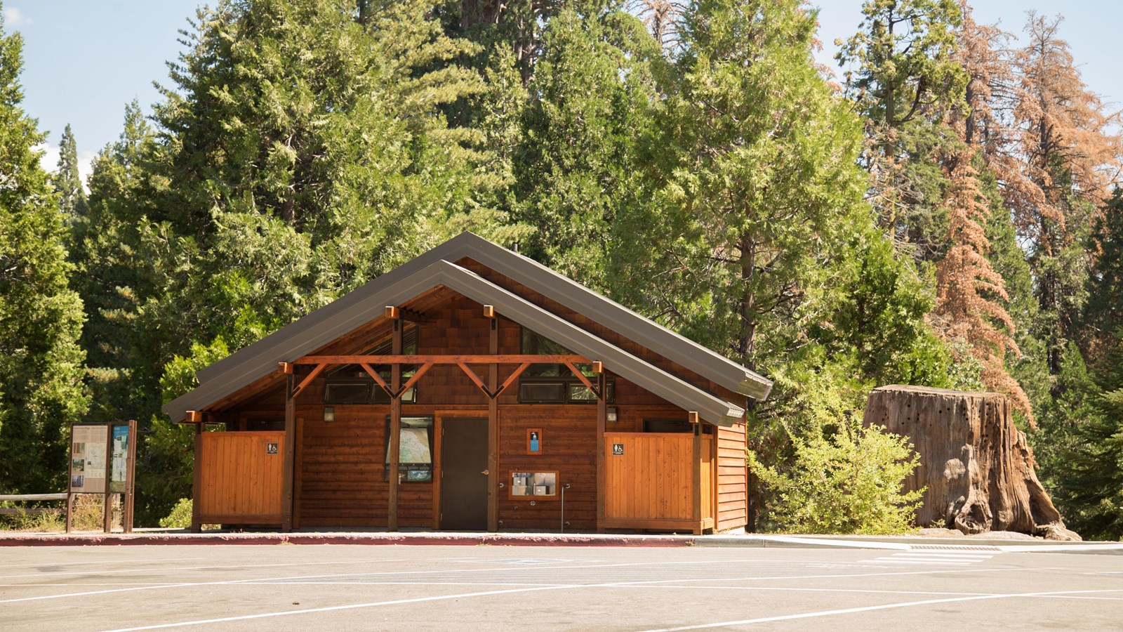 A wooden building stands in front of tall green trees. 