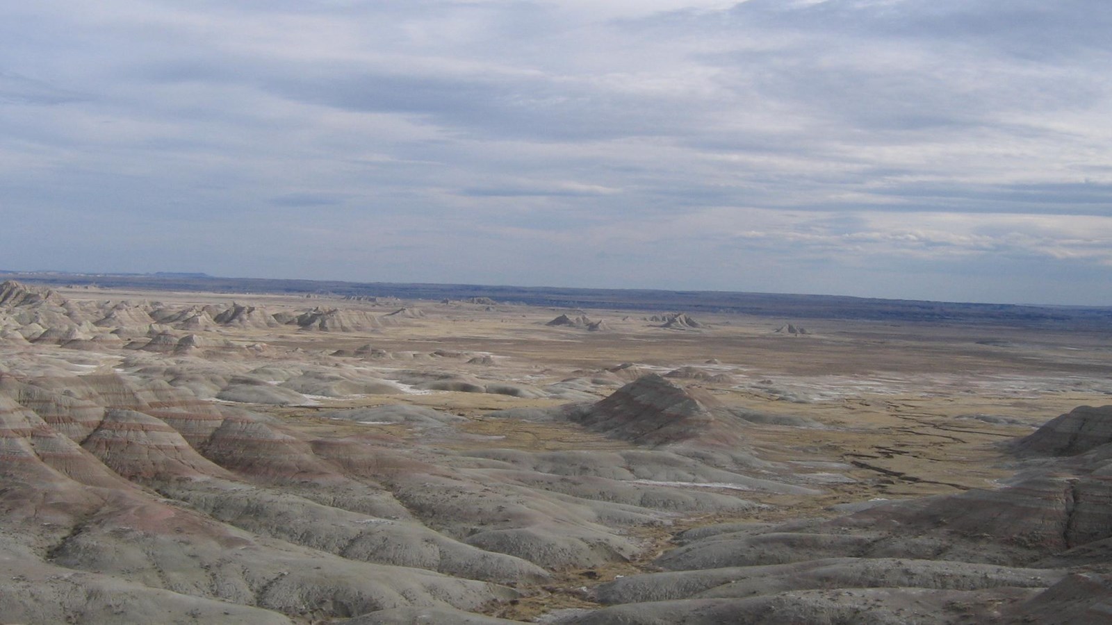 Rolling badlands buttes extend miles into the horizon under hazy blue sky.