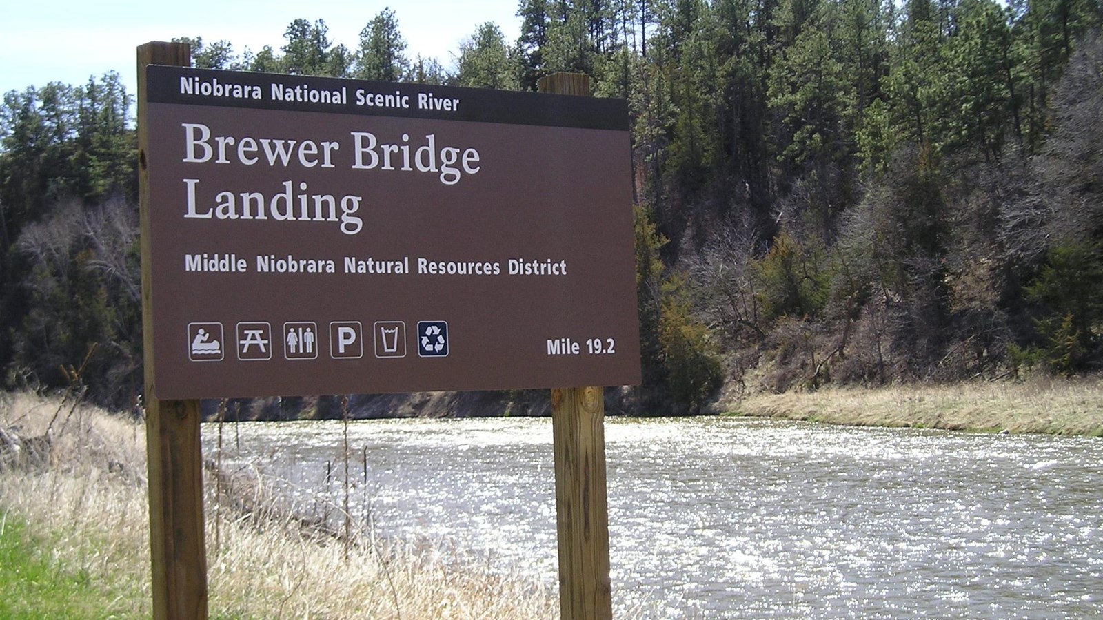 A brown sign on wood posts on a riverside.