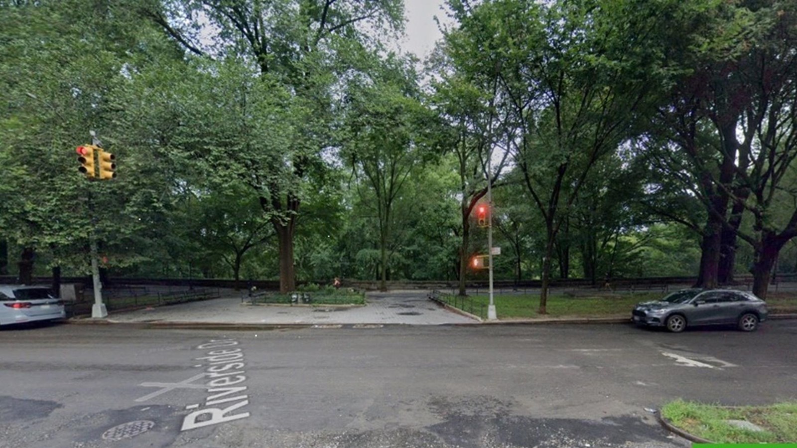 A sidewalk with traffic signals along a street with tree coverage.