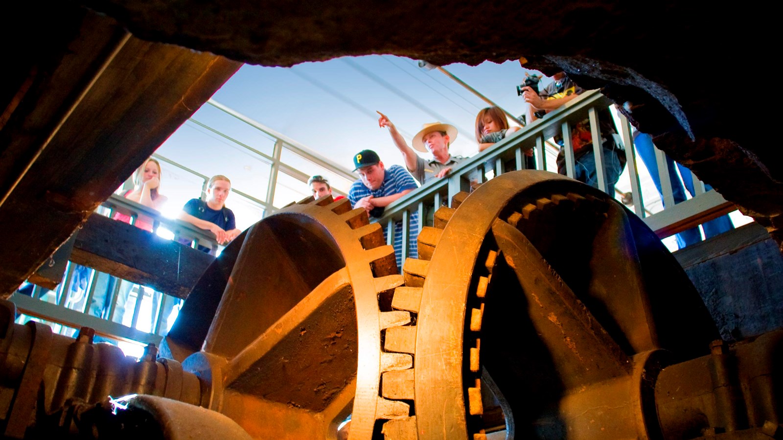 A group of visitors stand over a large set of gears in a historic mill