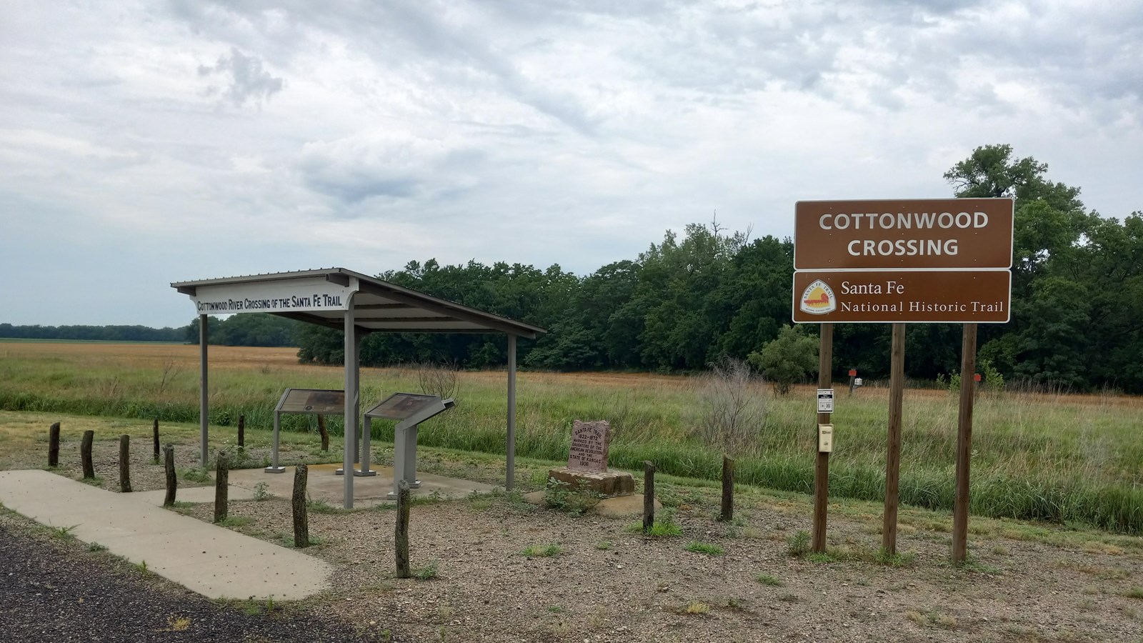 A parking area with a large brown sign in front of a grassy field.