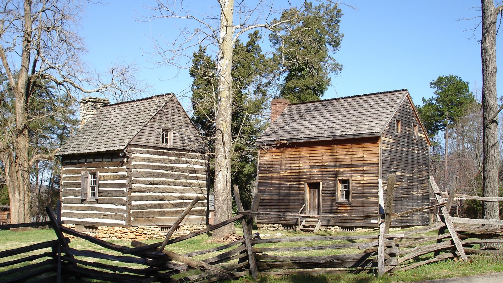 Behind a split rail fence, the Hoskins House and a separate kitchen building stand.