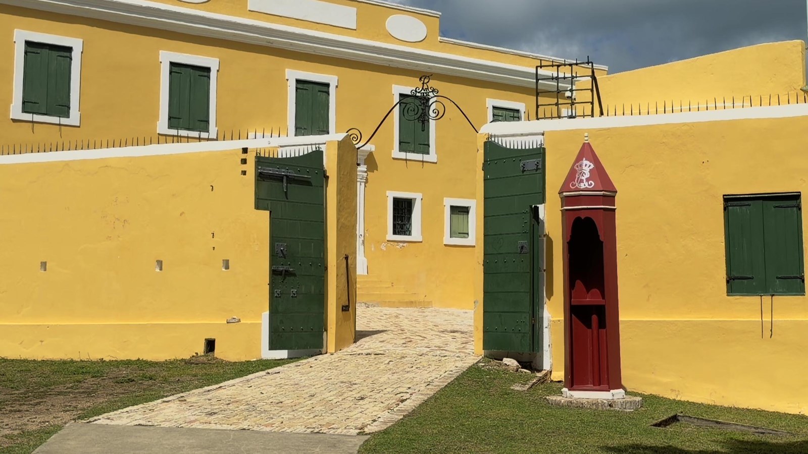 A colonial building with a guard post and open doors and a brick path leading into the fort.