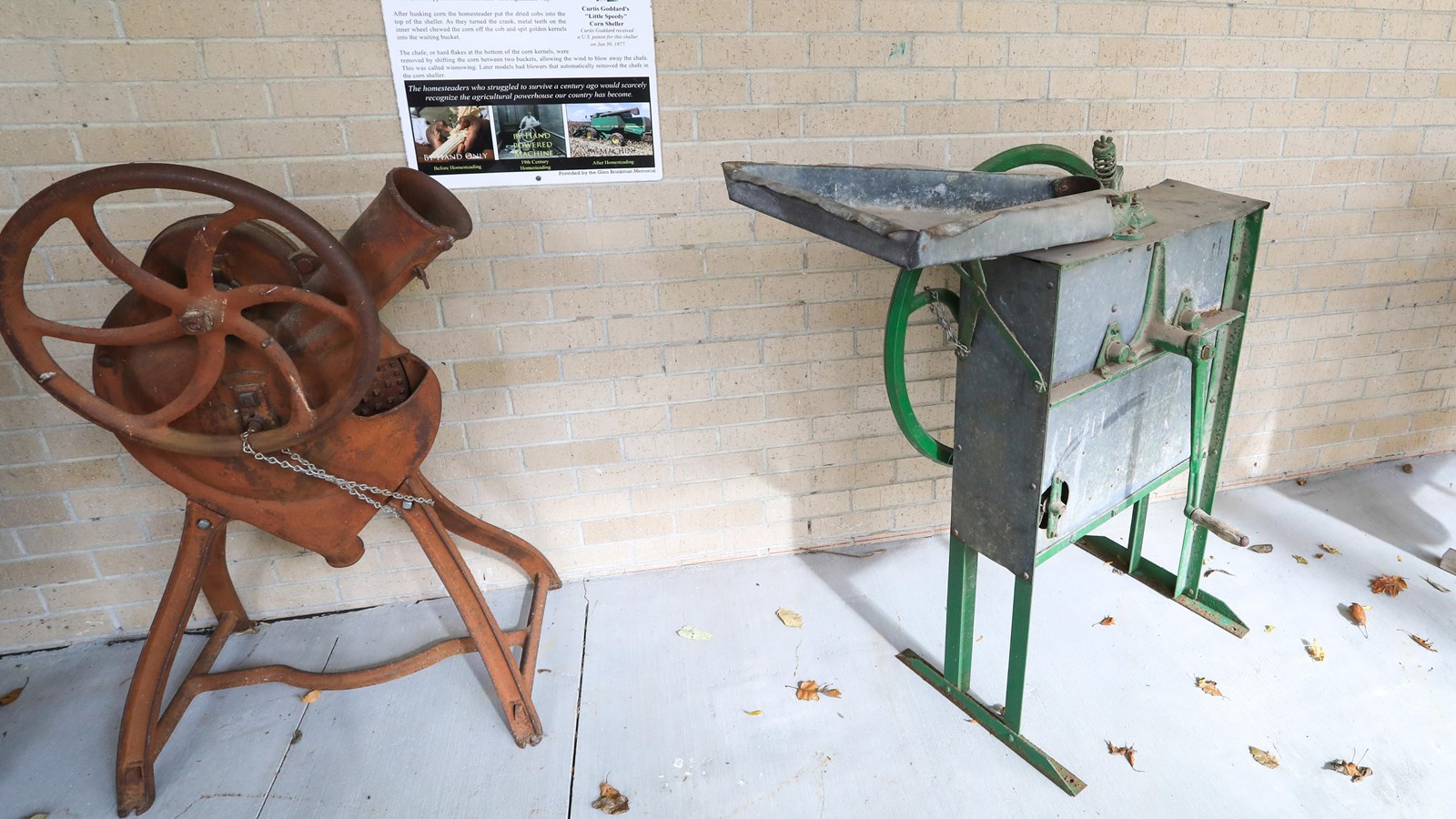 Two metal and wood machines are found in front of a brick wall with an informational panel.