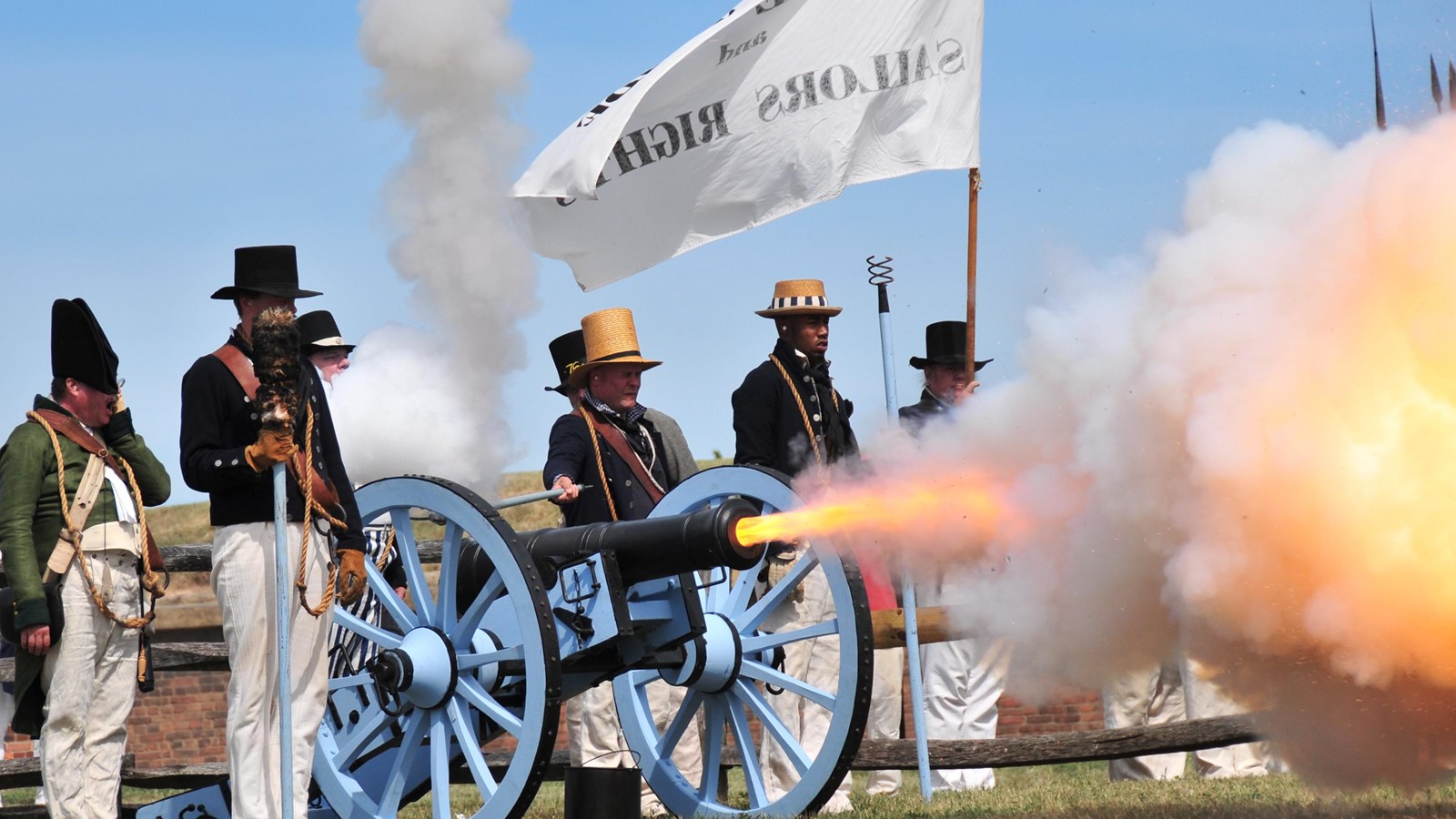 A group of people in period clothing stand next to a firing canon.