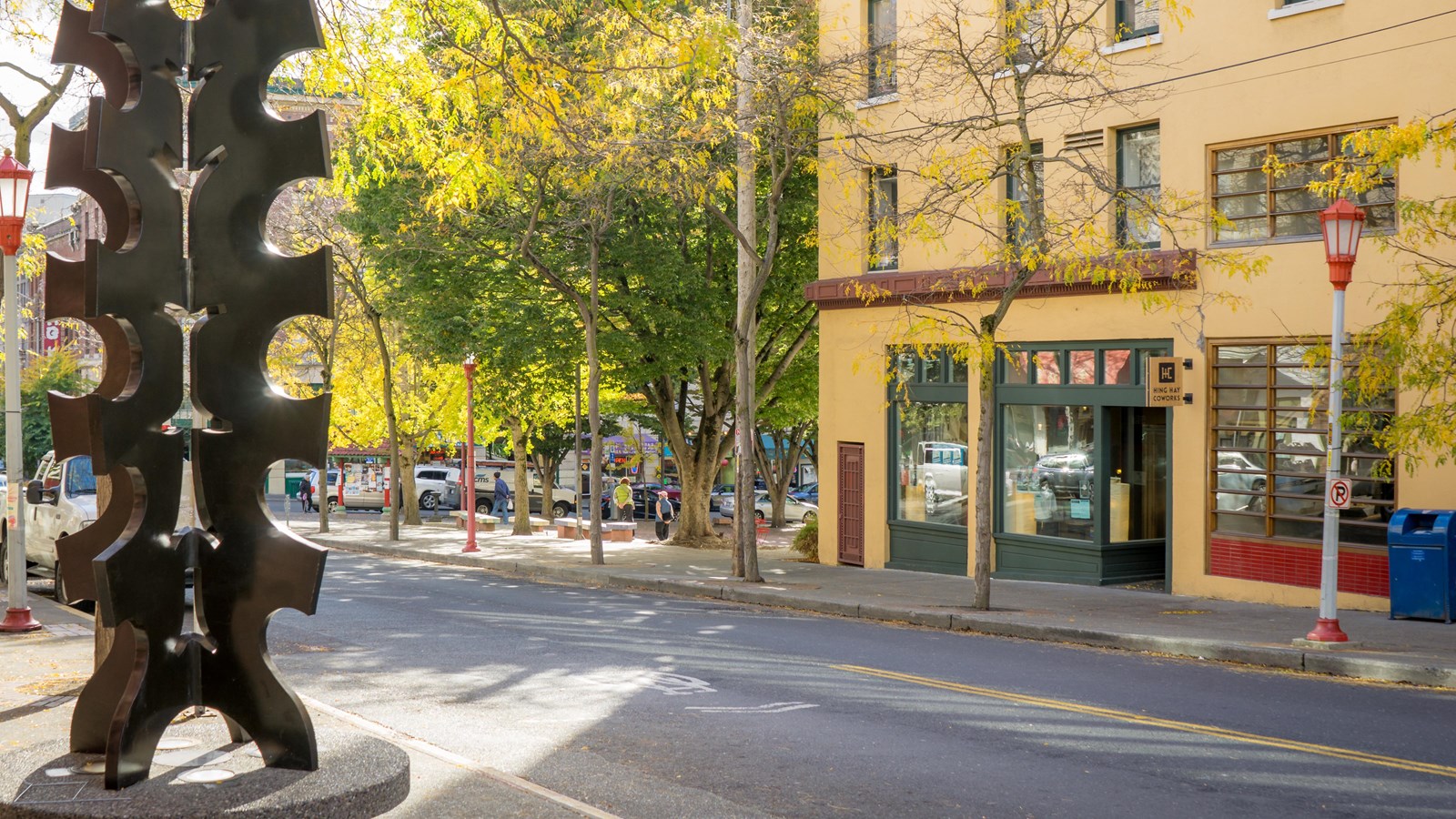 Historic yellow building adjacent to a modern metal sculpture surrounded by leafy trees.