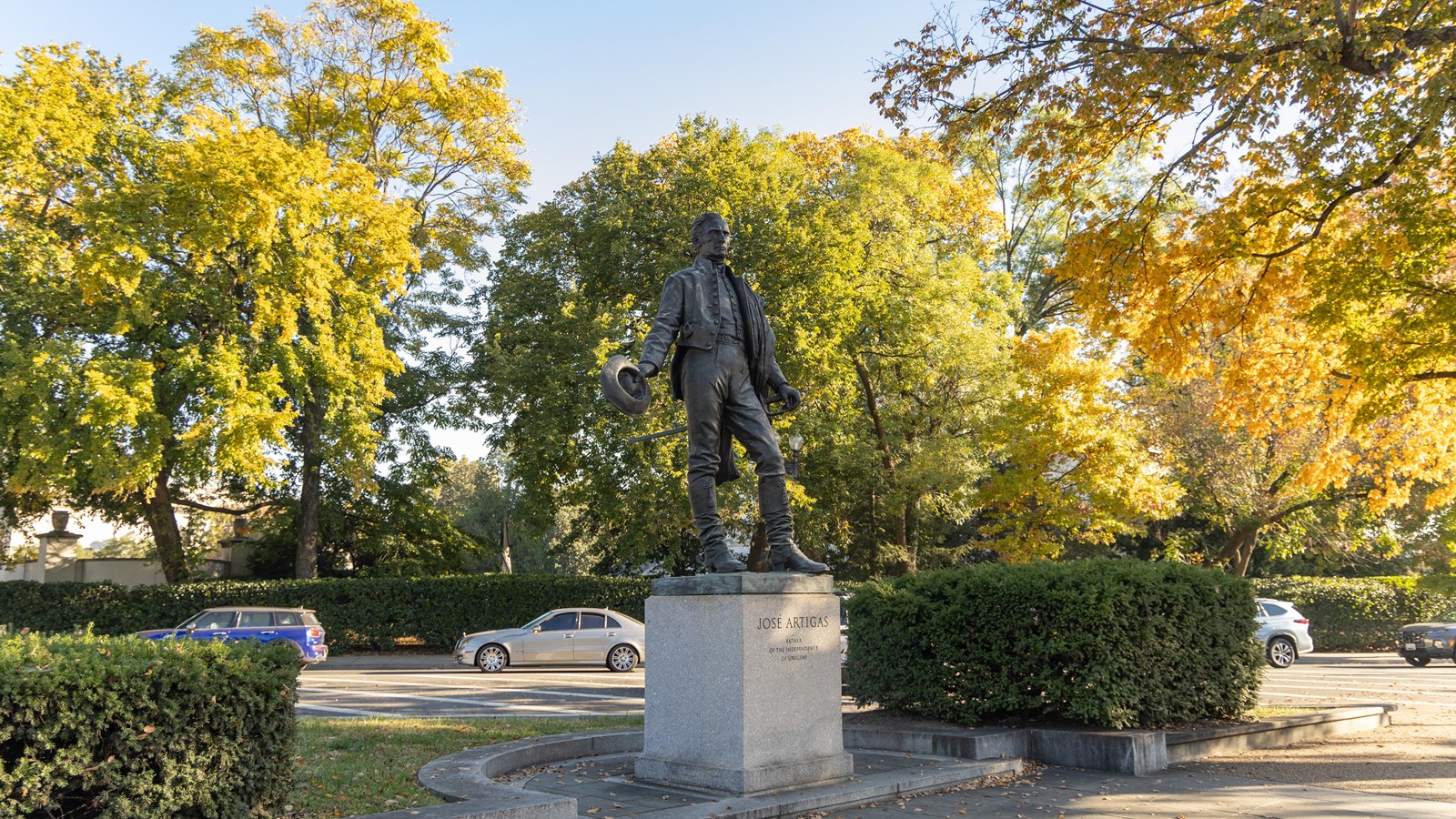 A tall memorial of a man holding a hat surrounded by orange and yellow leaves