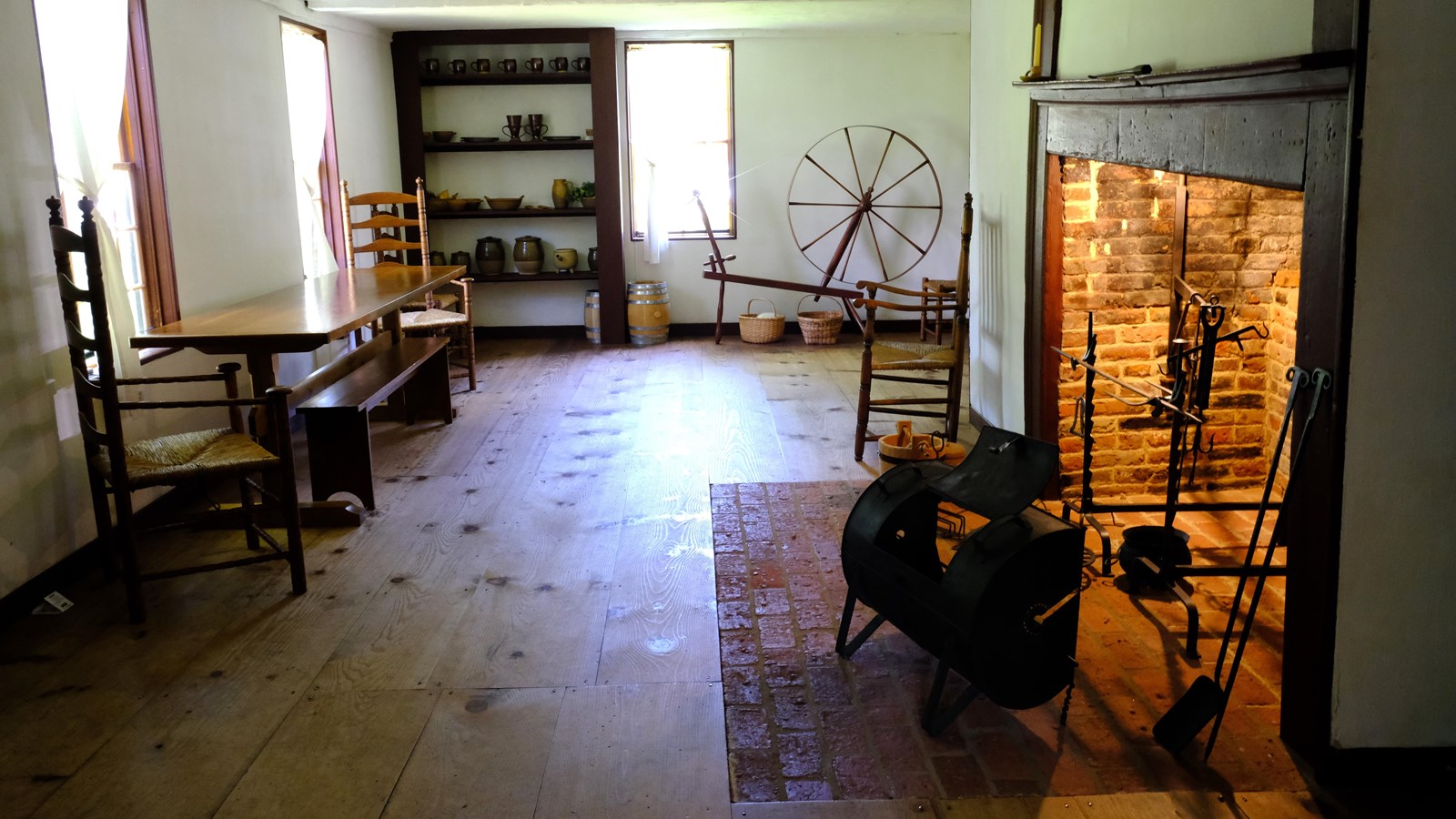 Large eighteenth-century room with dining table, chairs, large fireplace and cooking implements.