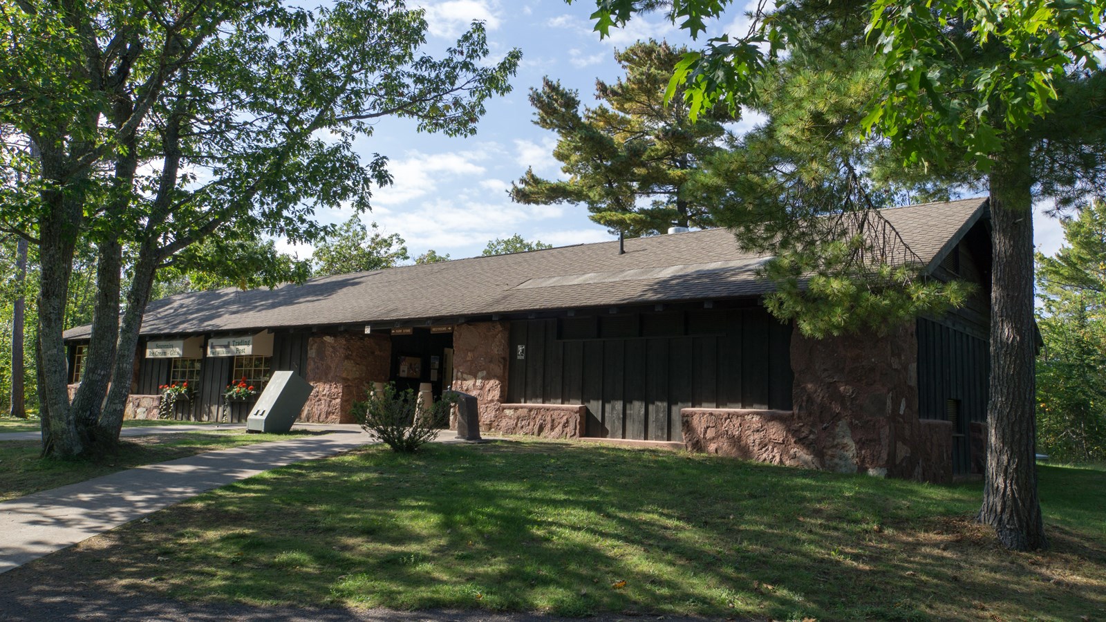 Summer scene of red sandstone building surrounded by trees and a sidewalk leading to the entrance.