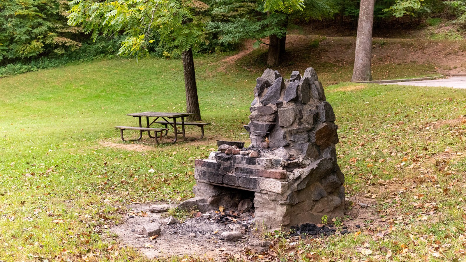 A stone fire pit and a picnic table in a grassy field. 