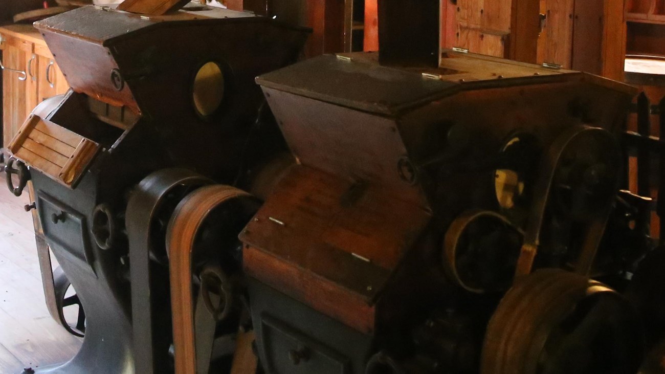Wooden and iron machines sit on a wood floor with cutes leading to them.