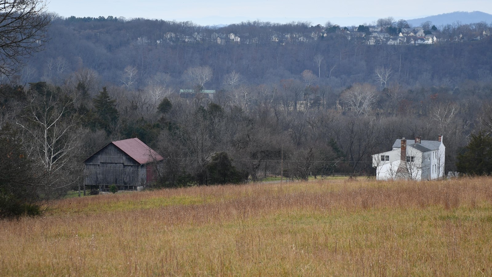 An 1800s farmhouse and barn are seen below from a hillside. 
