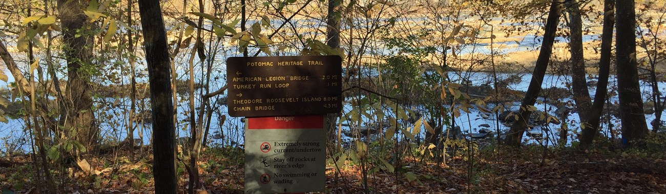 a wooden sign for the Potomac Heritage Trail in a forested riparian area