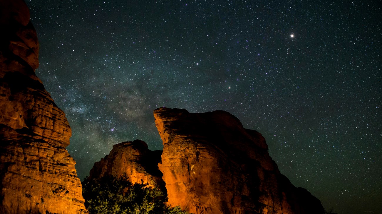 View of a dark night sky and the Milky Way with red peaks illuminated.