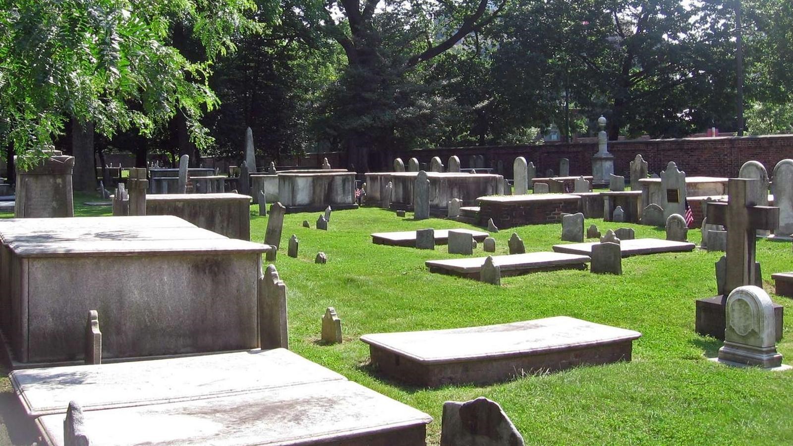 A color photo showing historic grave stones of numerous shapes and sizes in a field of green grass.