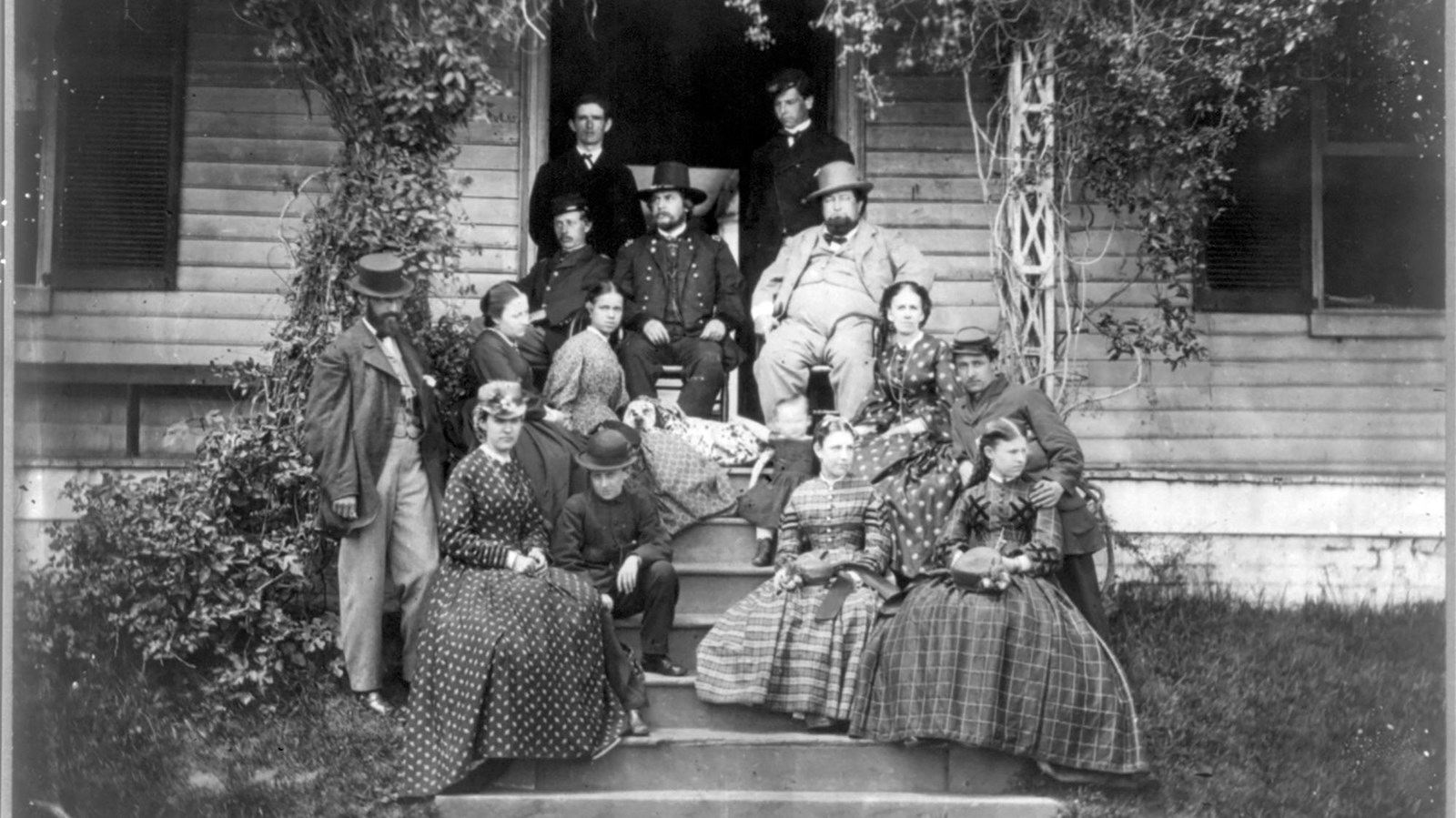 Historic, black and white photo of east side of home, with large group of people on front steps