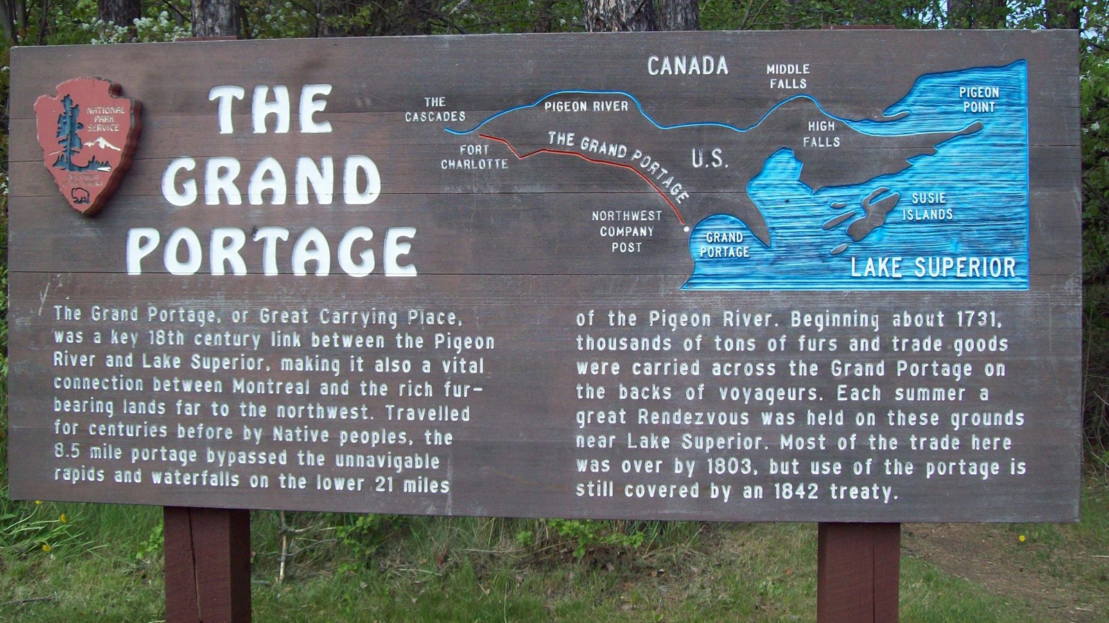 A wooden sign with a picture and text about the Grand Portage Trail