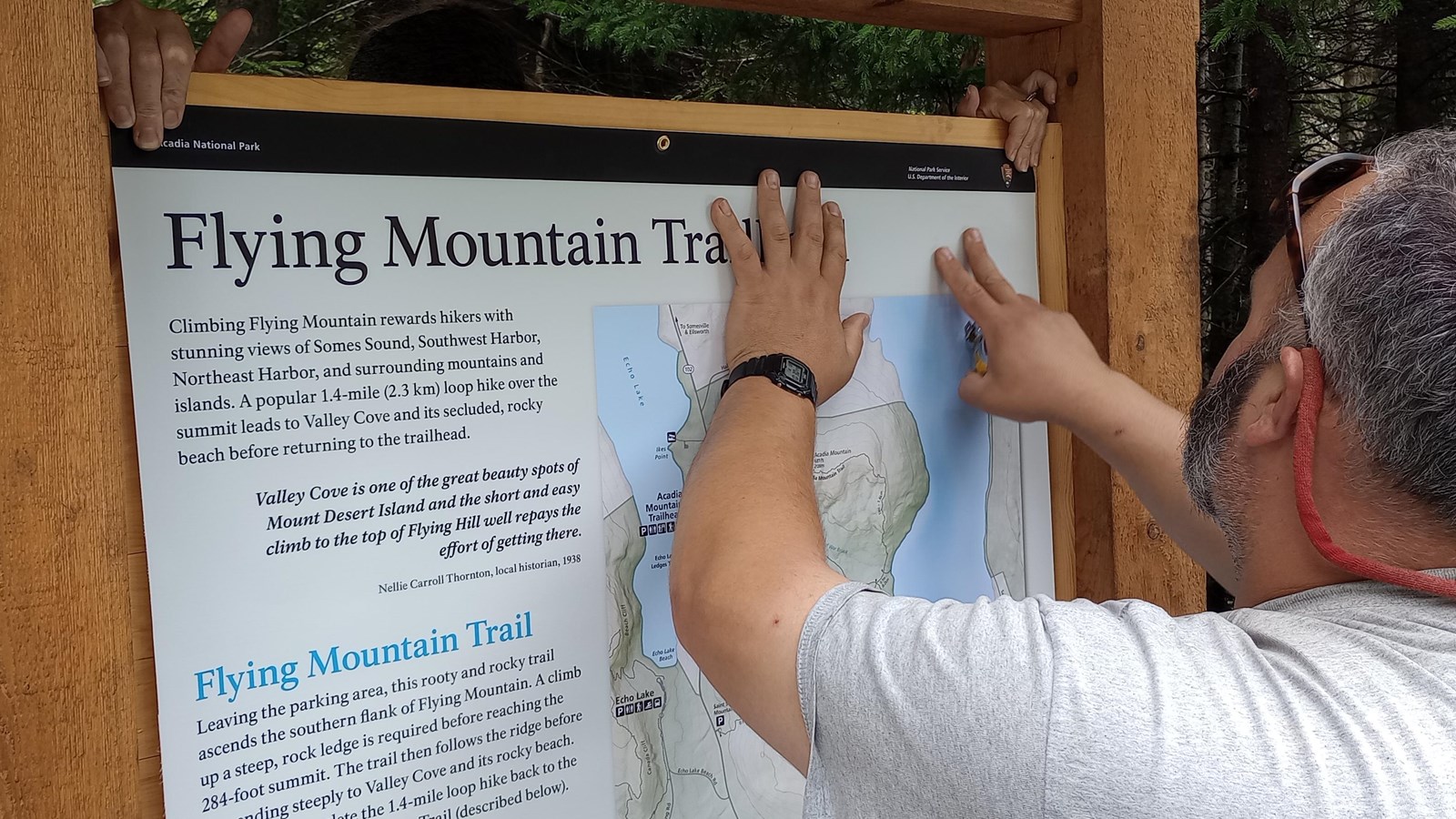 A man positions a printed panel inside the frame of a large timber trailhead structure