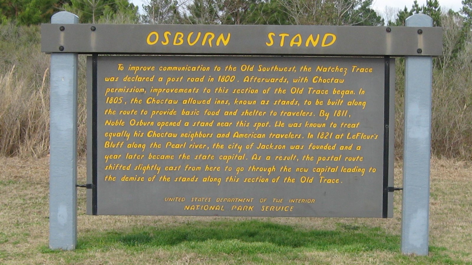 Wooden sign painted brown with yellow letters. Title of sign is