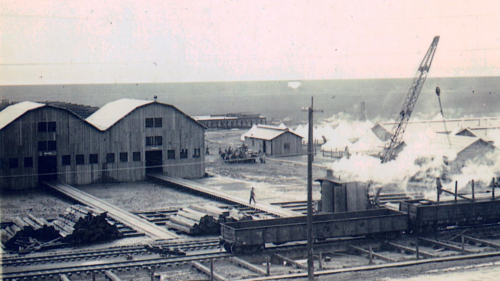 A black and white photo shows large wooden buildings connected to a railroad track.