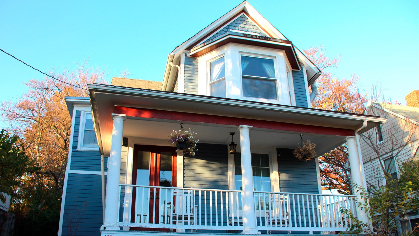A two-story blue wooden house with a front porch with white railing. 