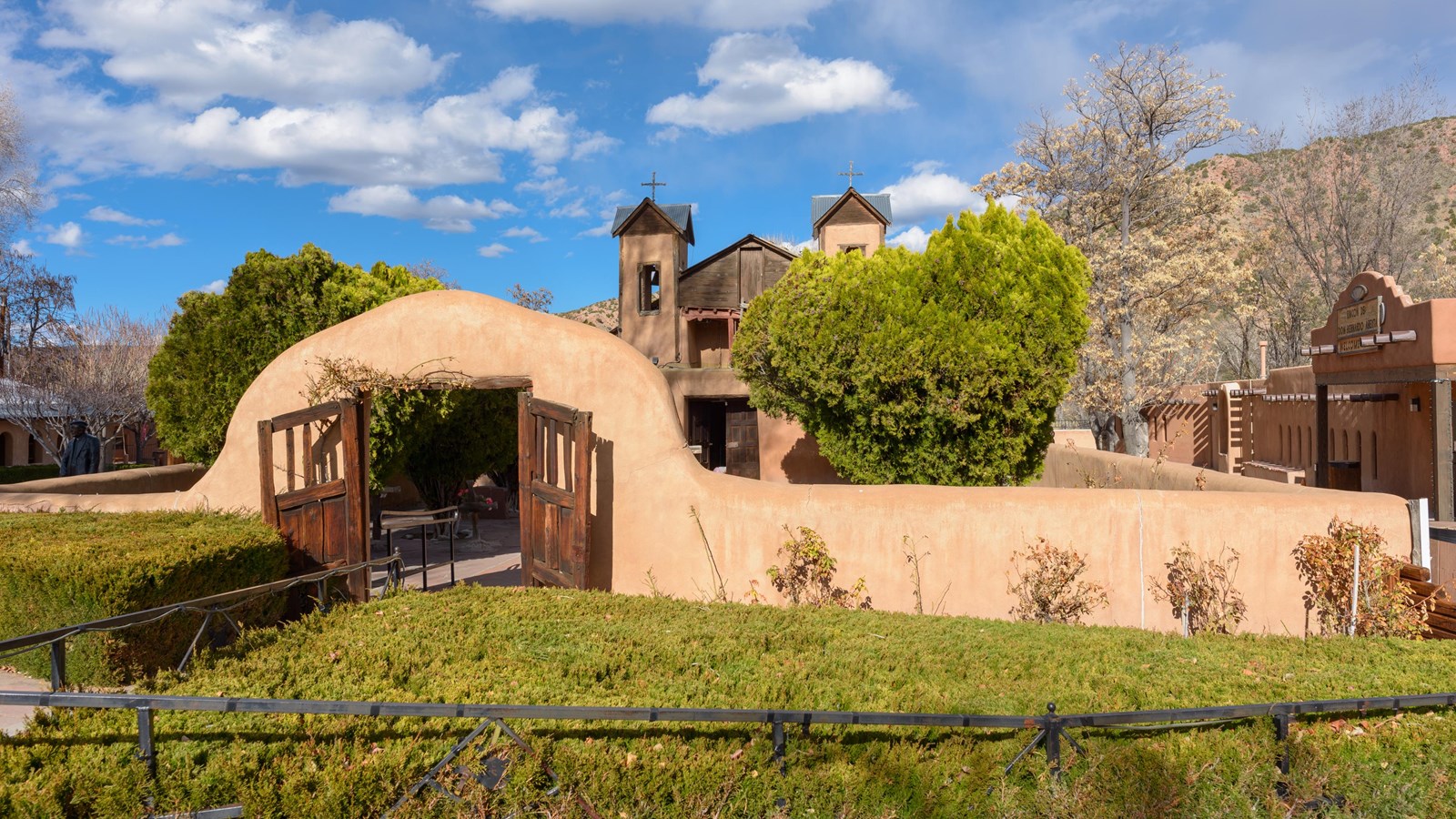 An adobe wall with an open gate, with an adobe church peeking out above the walls.
