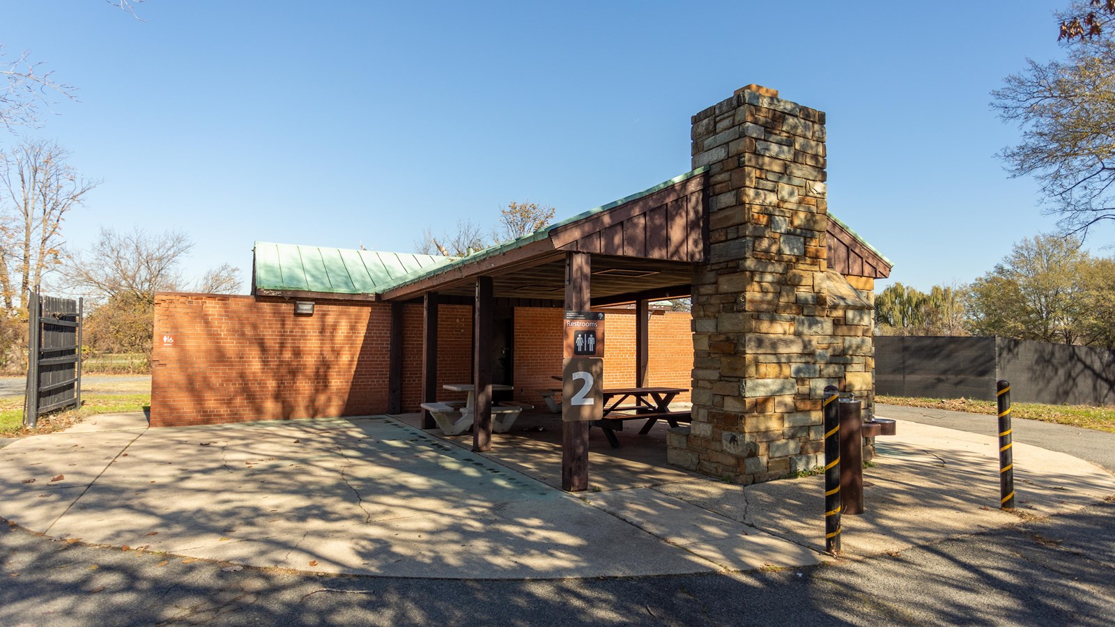 A brick building with an attached picnic shelter and sign for restrooms.