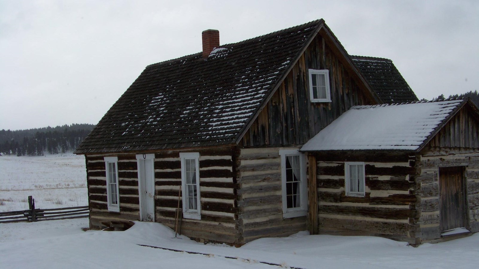 A 1 1/2 story log home with large wood beams and white chinking. A white door and two white windows