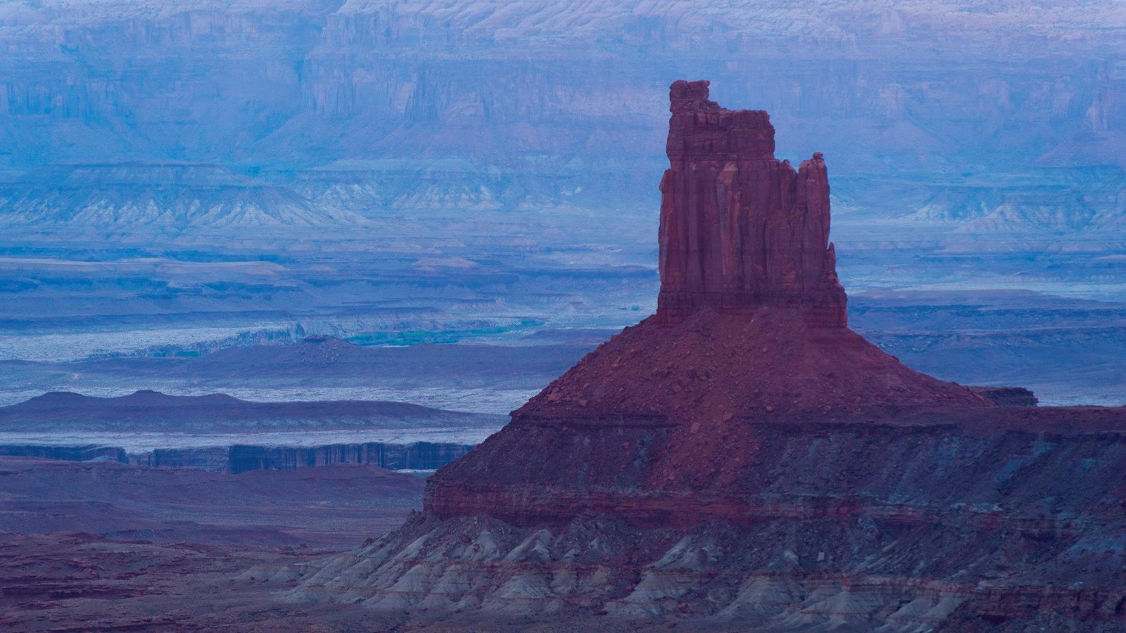 A dark red and brown sandstone feature that resembles a group of candles juts from the valley floor.