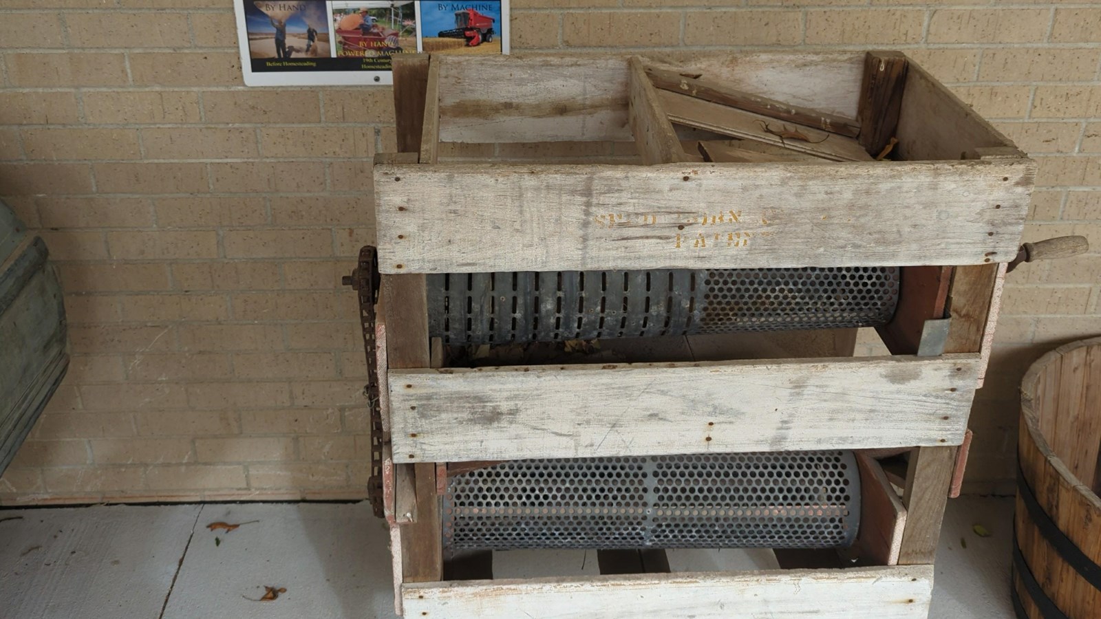 Machine made of wood frame with metal rotating cylinders with holes in front of informational panel.