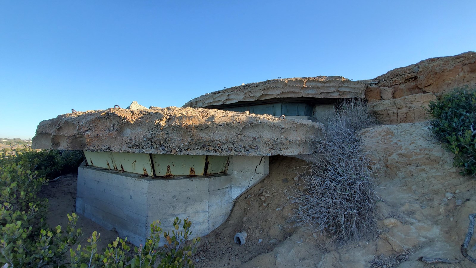 Rounded structure on a sandy hillside. Two offset tiers on structure with horizontal slits.