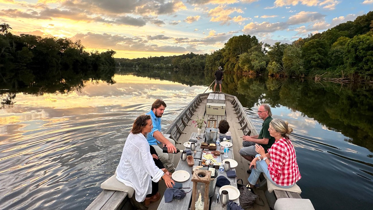 People dining on a wooden boat on a calm river during sunset.