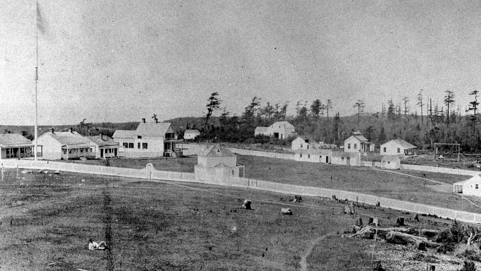 Black and white photo of numerous military buildings and men surrounded by a picket fence