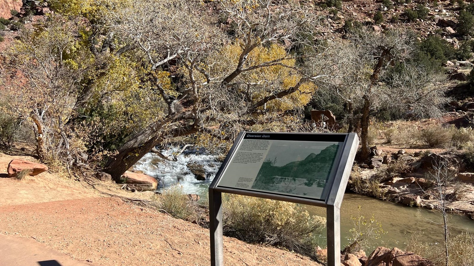 Photo of a sign in front of the Virgin River, surrounded by trees.