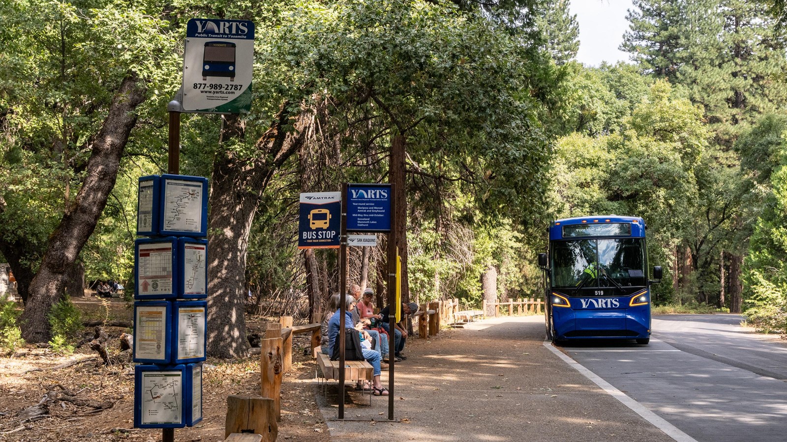 Several transit signs on multiple metal posts and a large blue bus parked